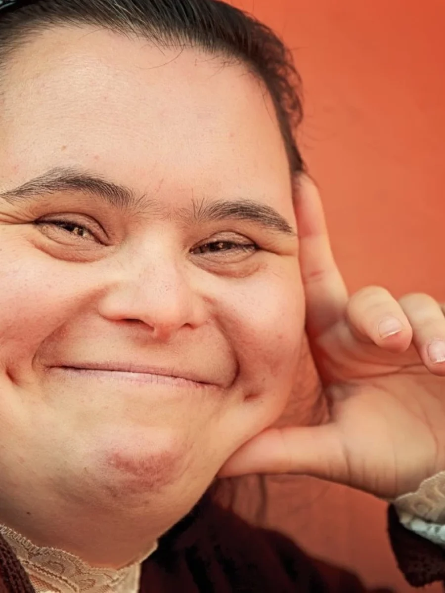 Girl with down syndrome leaning with head in hand and smiling at camera